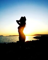 Silhouette woman standing on beach against clear sky during sunset