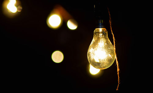 Close-up of illuminated light bulb hanging against black background