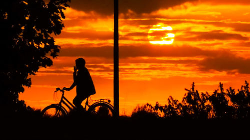 Silhouette person riding bicycle against sky during sunset