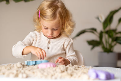 Cute happy blonde,curly-haired toddler,baby girl playing with kinetic sand.motor skills concept.