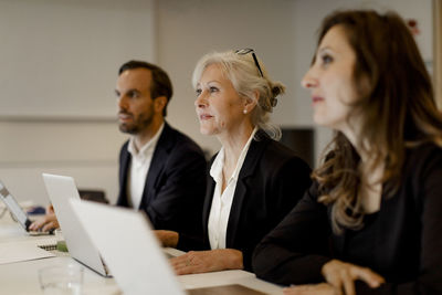 Male and female executives using laptops at conference table in office meeting