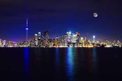 Illuminated buildings by sea against sky at night