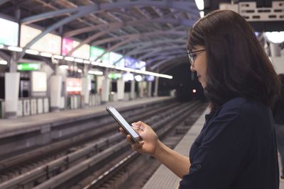 Side view of man using mobile phone at railroad station