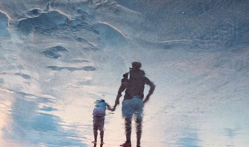 Reflection of father and daughter in sea