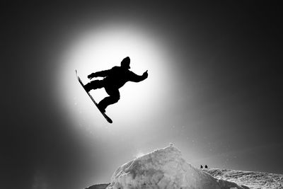 Silhouette people jumping on rock against sky