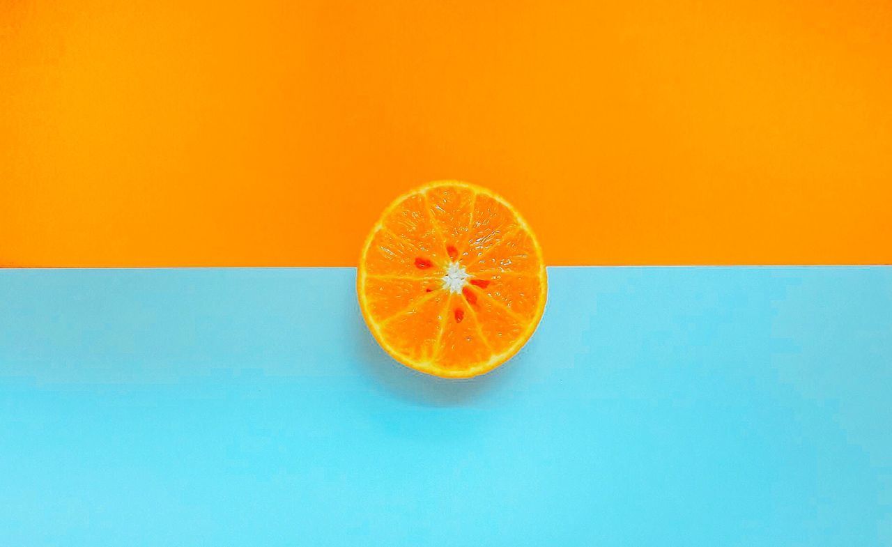 CLOSE-UP OF ORANGE SLICE ON TABLE AGAINST YELLOW BACKGROUND