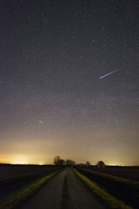 Road amidst field against clear sky at night