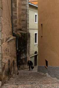 Rear view of man walking in alley amidst buildings
