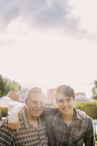 Portrait of happy grandfather and grandson with arms around against sky