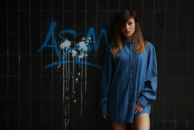 Portrait of young woman wearing blue shirt while standing against wall