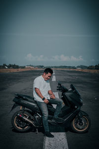 Young man riding motorcycle on road against sky