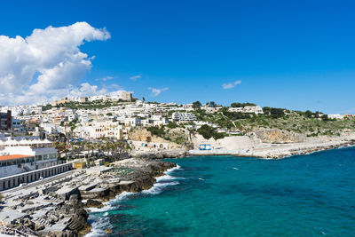 Aerial view of townscape by sea against blue sky