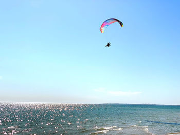 Person paragliding over sea against clear sky