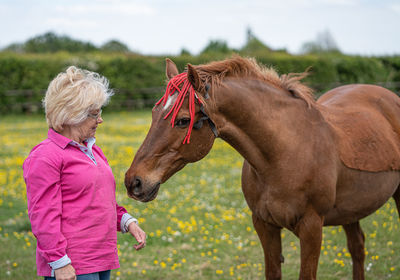 Senior woman standing by horse on field