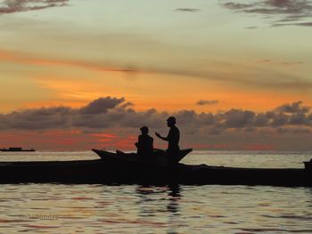 Silhouette men in sea against sky during sunset