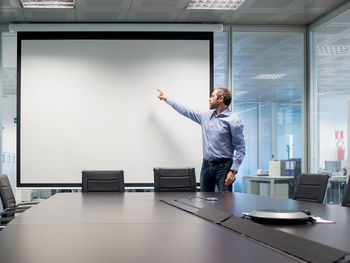 Businessman pointing towards projection screen while standing in board room at office