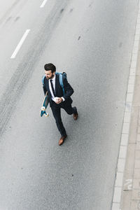 Businessman with takeaway coffee and skateboard walking on the street