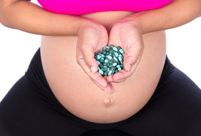 Midsection of pregnant woman holding capsule against white background