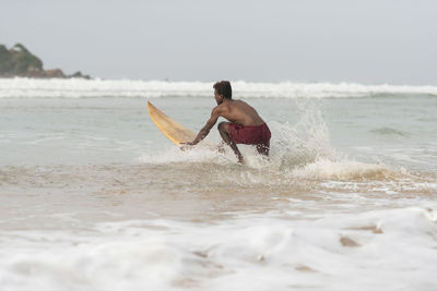 Shirtless man surfing in sea against sky