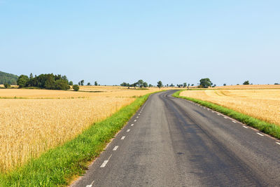 Road amidst field against clear sky