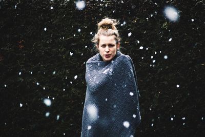 Portrait of young woman standing at yard during snowfall