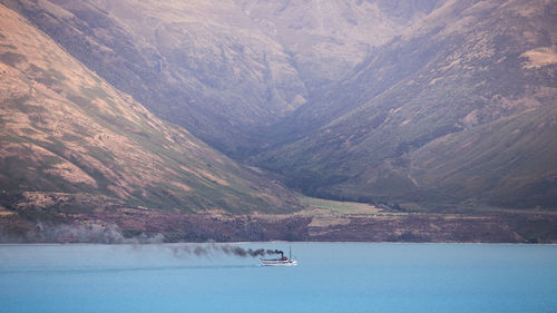 Boat sailing on sea by mountain