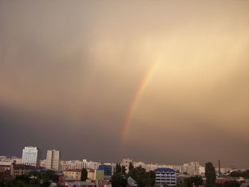 Rainbow over buildings in city against sky during sunset