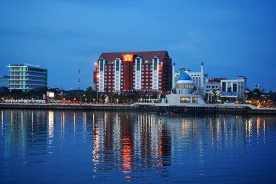 Buildings by river against blue sky