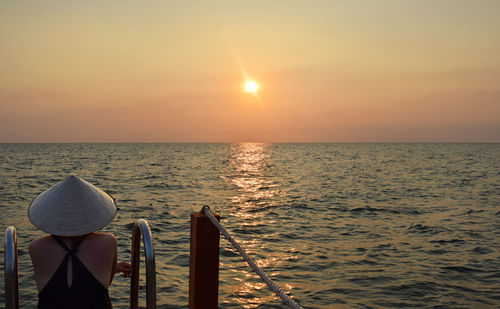 Rear view of woman in sea against sky during sunset