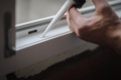 A young man squeezes silicone into a hole in a window frame.