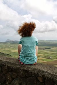 Rear view of woman sitting on field against cloudy sky