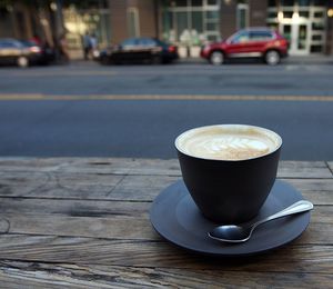 Cappuccino cup on wooden table by street