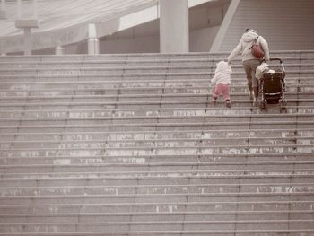 Low angle view of mother holding child and baby carriage on steps at airport