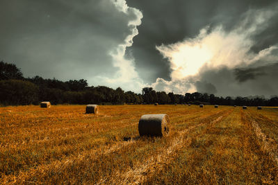 Hay bales on field against dramatic  sky