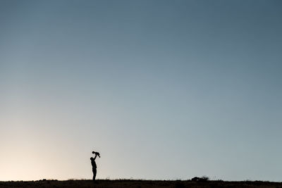 Silhouette father with child standing on field against clear sky during sunset