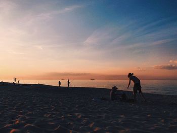 Silhouette women playing on beach against sky during sunset