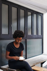 Young man looking at camera while sitting on window