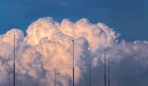Low angle view of masts against cloudy sky