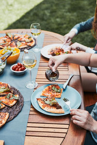 Family and friends having meal - pizza, salads, fruits and drinking white wine during summer picnic