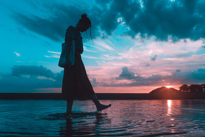 Silhouette woman standing by sea against sky during sunset