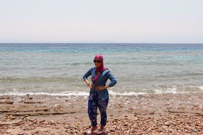 Full length of woman standing on shore at beach against clear sky