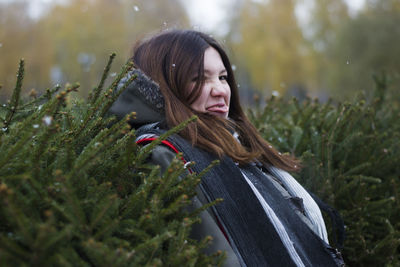 Playful woman sticking out tongue by plants during winter