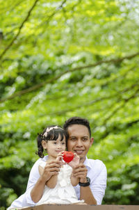 Smiling father and daughter with heart shape toy looking away while sitting in park