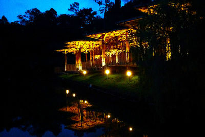 Illuminated buildings by lake against sky at night