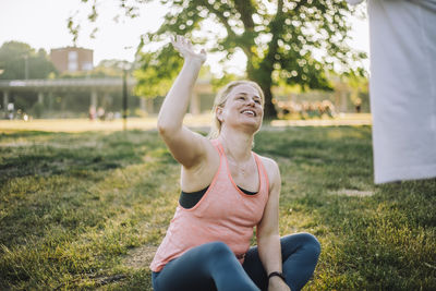 Smiling woman giving high-five to friend while sitting on grass at park