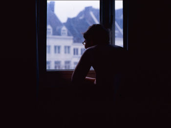 Silhouette man looking through window at home