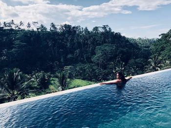 Shirtless man swimming in infinity pool against forest