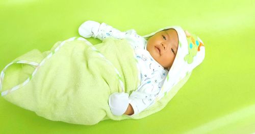 High angle view of newborn baby wrapped in blanket on green table