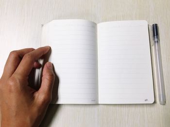 Cropped hand with book and pen on table