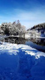 Frozen lake by trees against blue sky